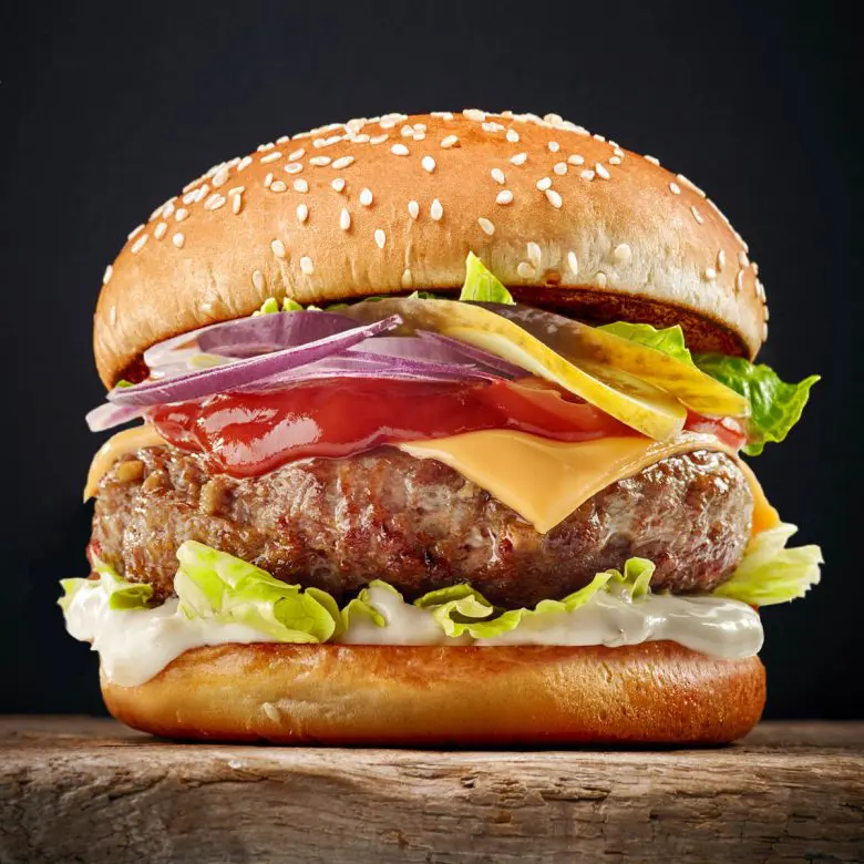 Cheeseburger stacked with lettuce, tomatoes, pickles, red onions mayo and ketchup