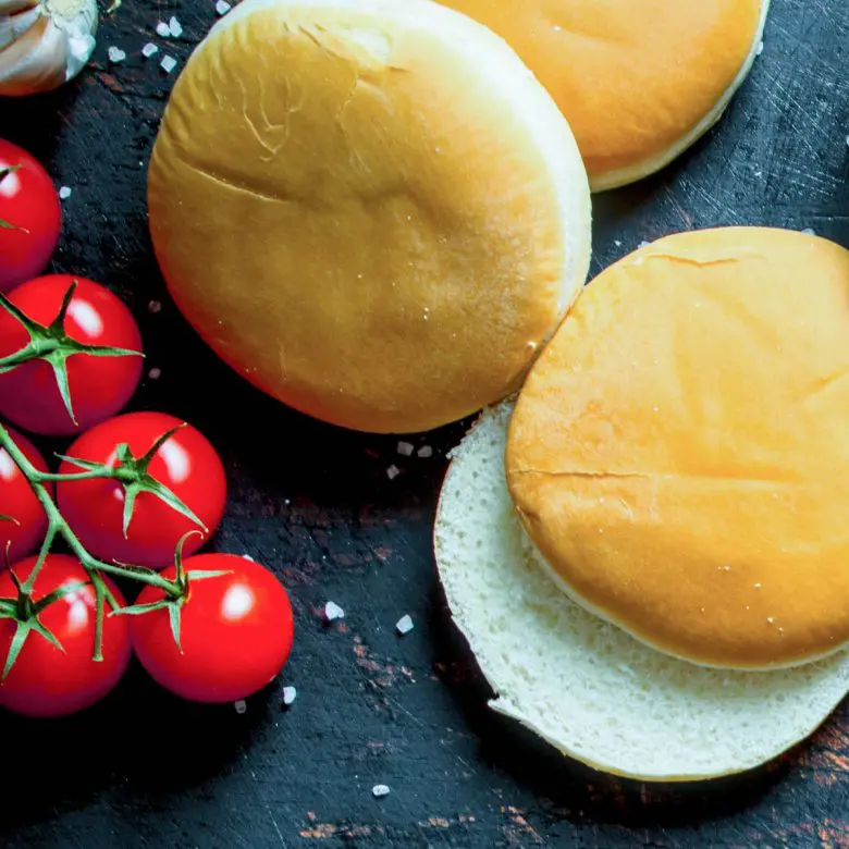 2 classic hamburger buns and a vine of grape tomatoes next to them and coarse salt sprinkled around them.