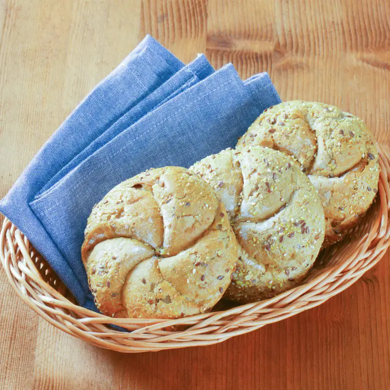 3 Kaiser rolls on a wicker basket with a blue cloth napkin.