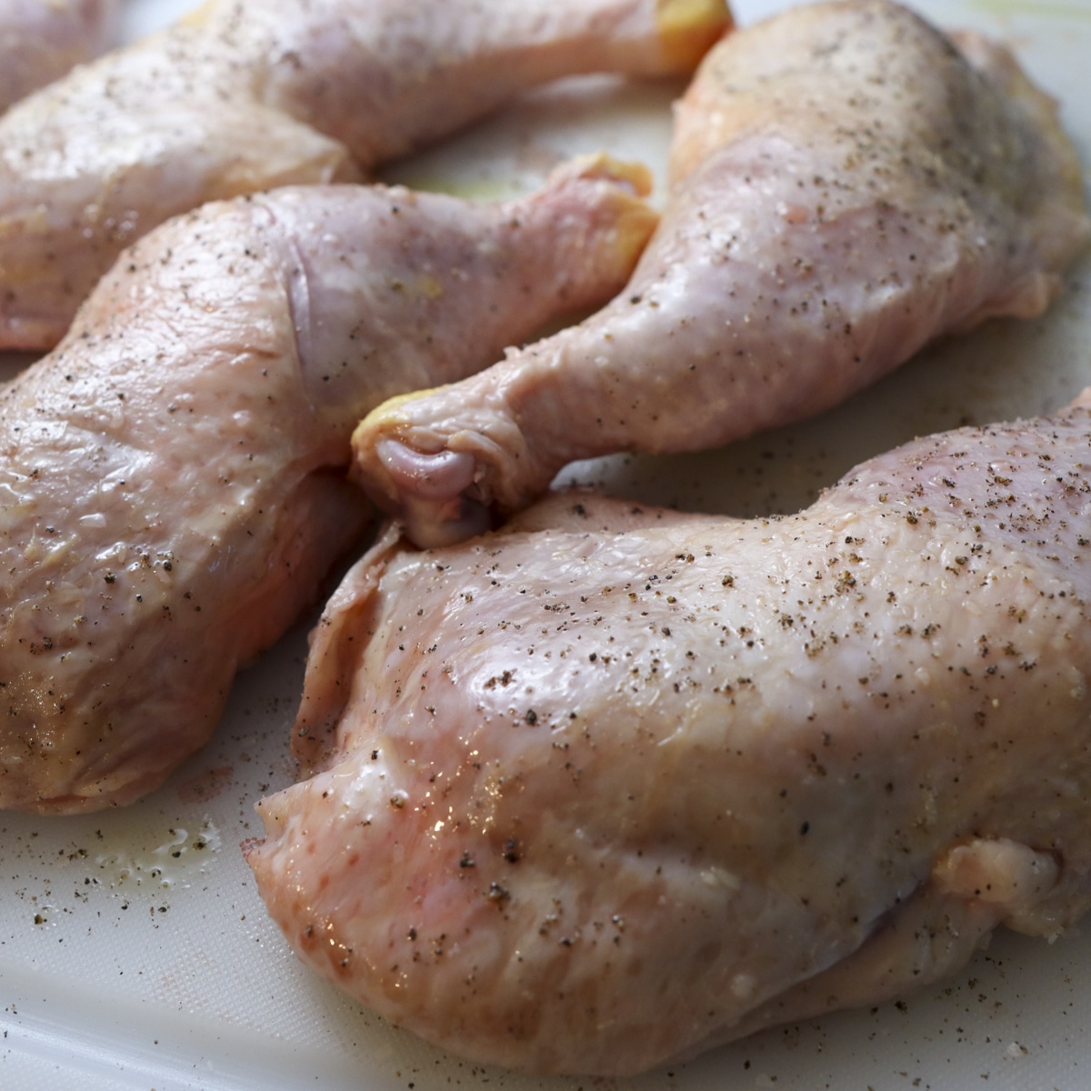 oil and pepper and salt chicken leg quarters on a cutting board
