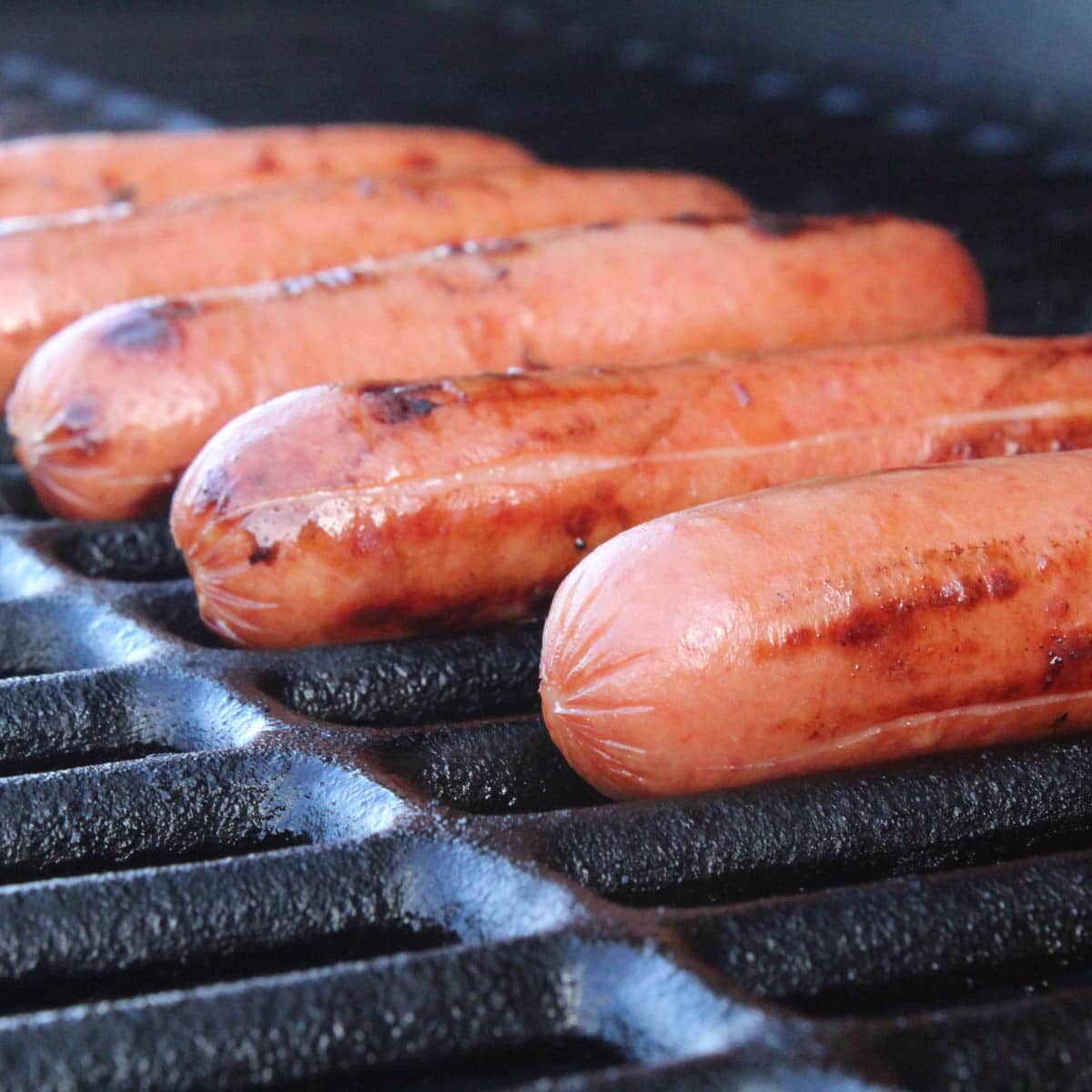 Grilled hot dogs cooking on a grill with grill marks on them.