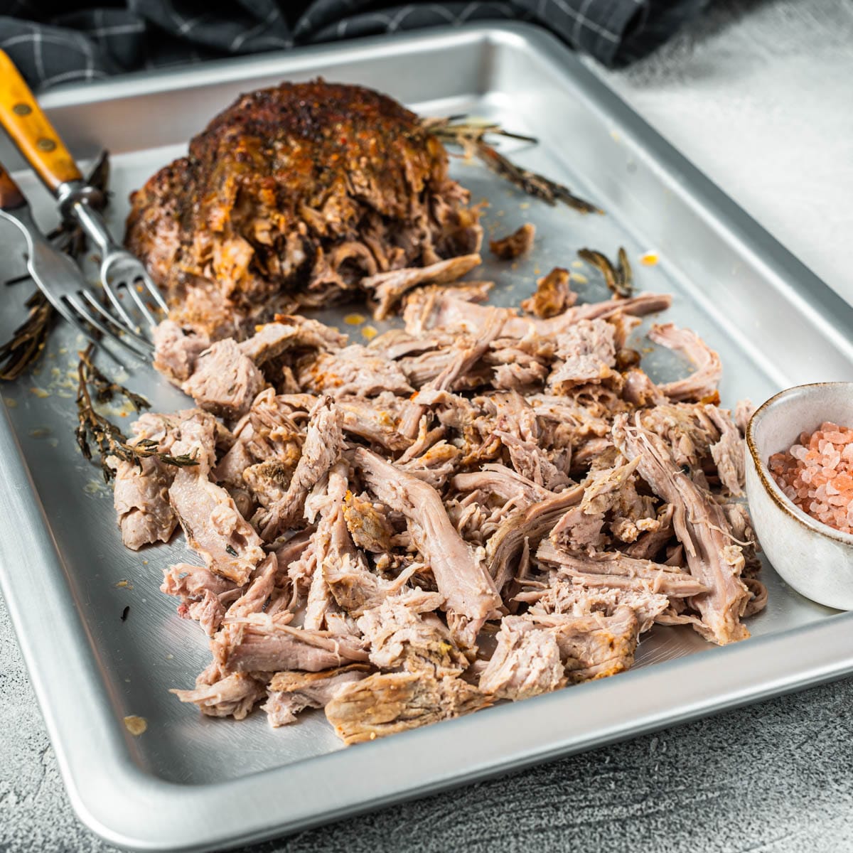 Sheet pan with pulled pork, two forks and a small bowl of salt on the pan.