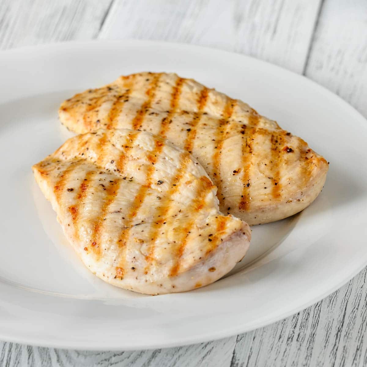 Two grilled chicken breast on a white plate with a whitewash background