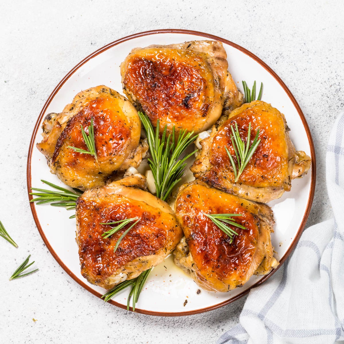 Five grilled chicken thighs on a round plate with sprigs of rosemary