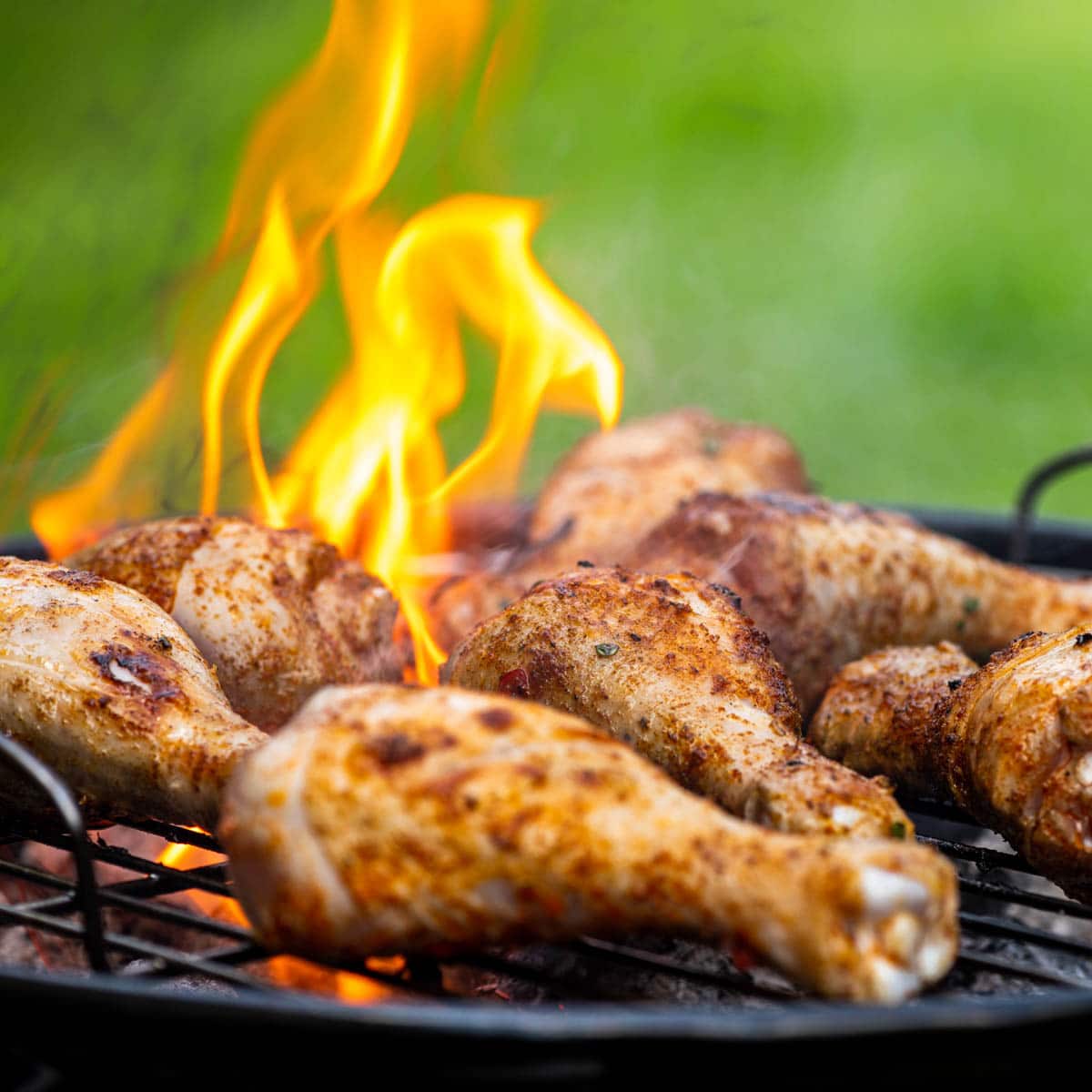 Chicken drumsticks on a charcoal grill with flames.