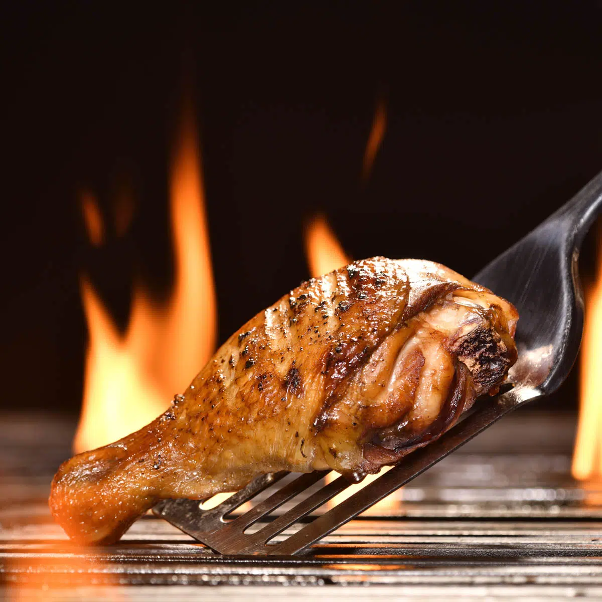 Grilled chicken leg on a flaming grill.