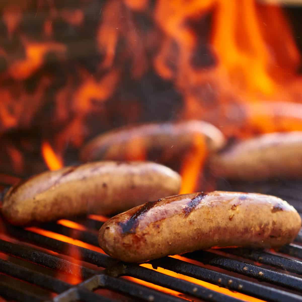 Brats on the grill with flames.