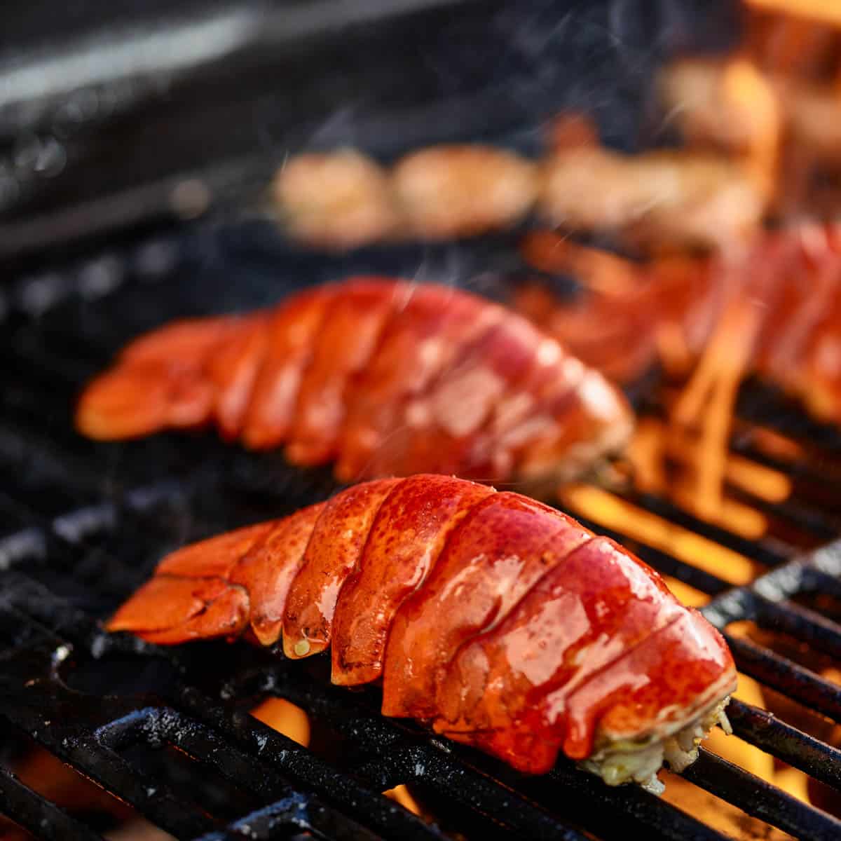 Lobster tails on the grill with flames.