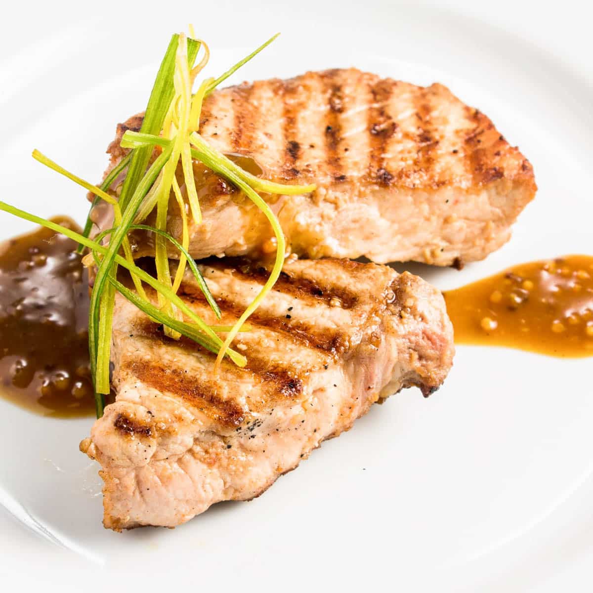 Grilled pork chops on a white plate with mustard sauce.
