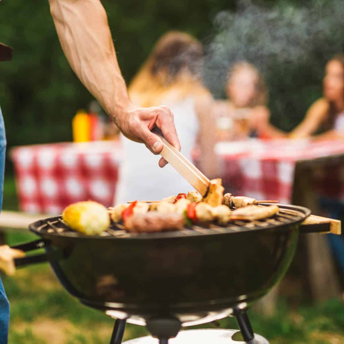 Man grilling on a charcoal grill with a a picnic table in the background