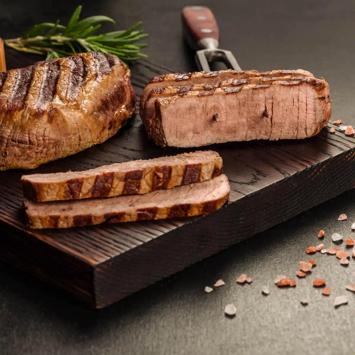 Sliced grilled steak on a dark slab of wood.